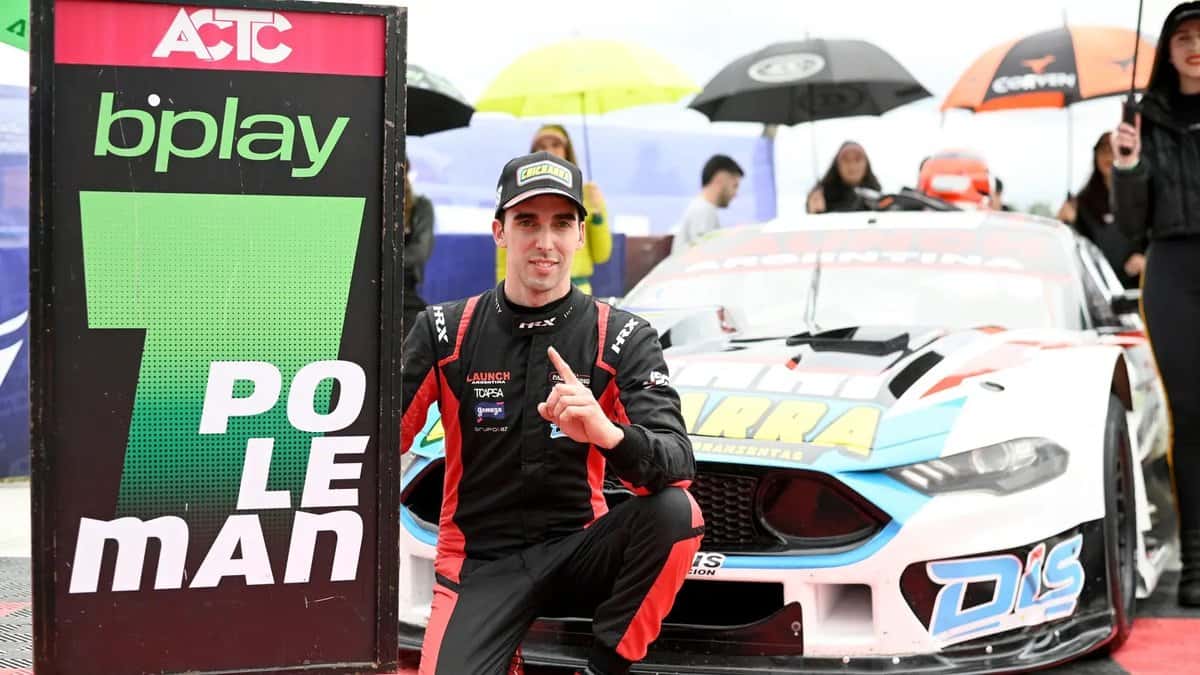 Juan Sebastián Gallo, con el buzo negro y rojo de su equipo, festeja agachado junto al cartel de poleman y a su Ford Mustang blanco en Rosario