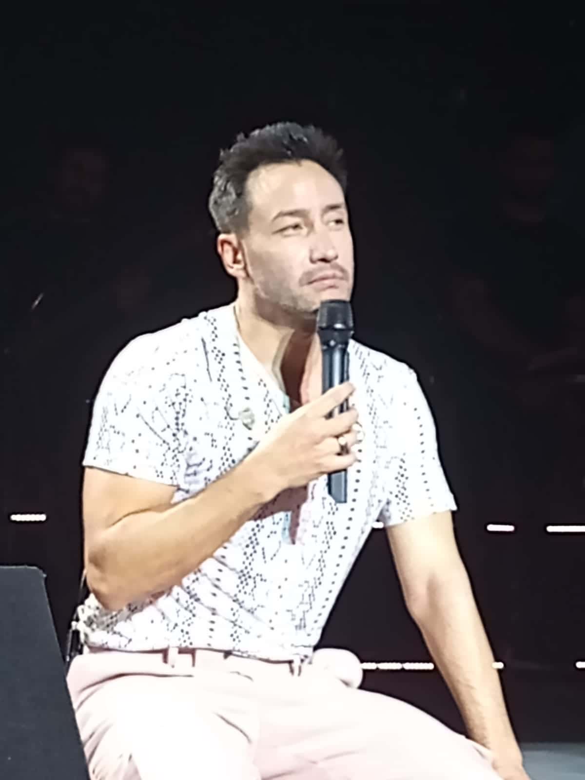 Luciano Pereyra, sentado en el escenario con camisa blanca y micrófono en la mano, durante un recital en el Luna Park en 2021 (foto de archivo)